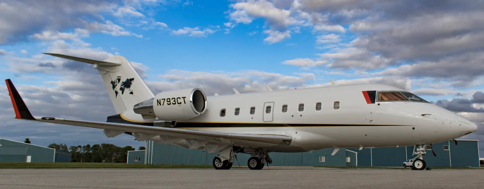 Large white jet with blue and red accents in the foreground with the blue green hangars in the rear